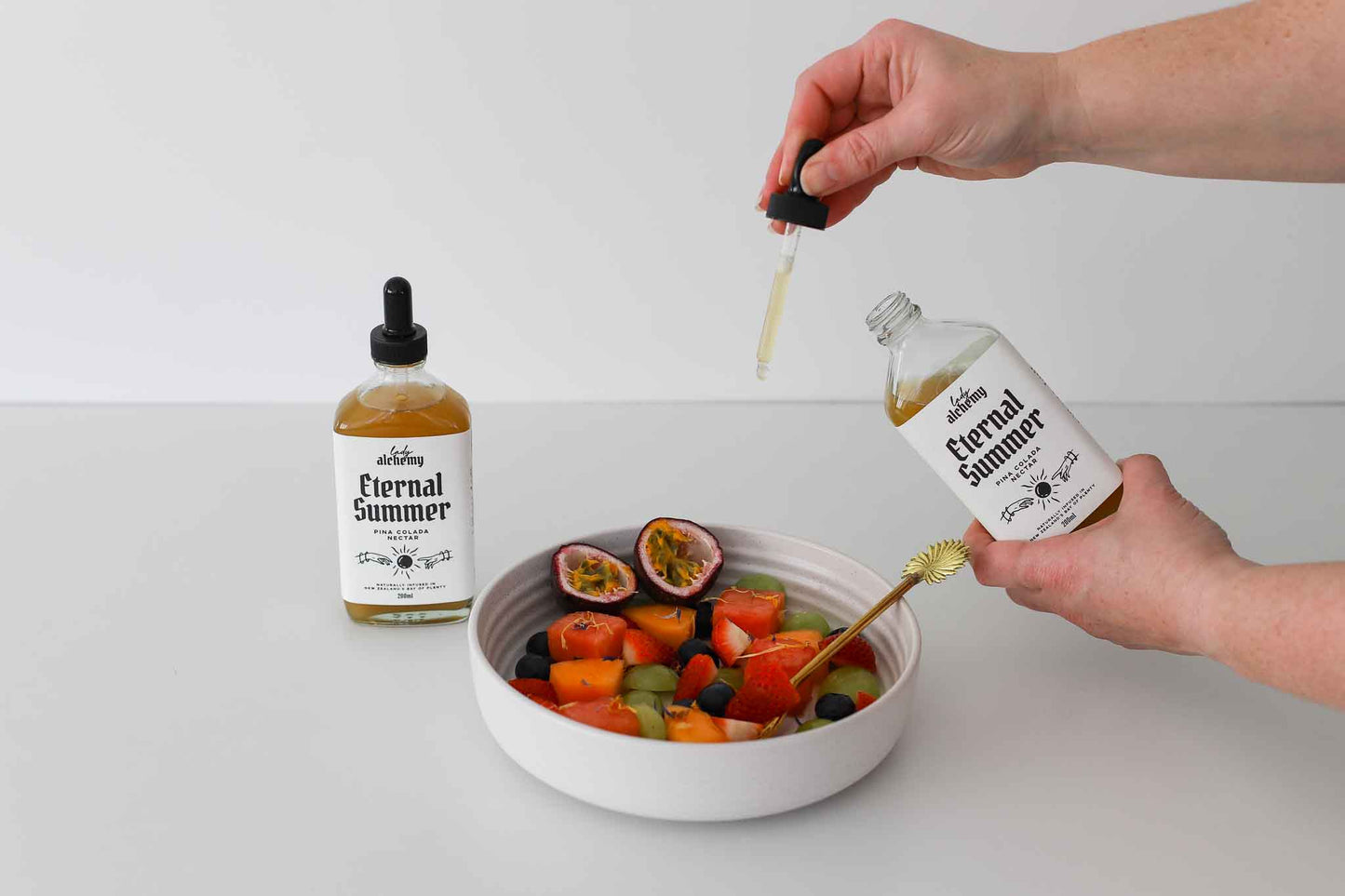 Person drizzling Pina Colada Nectar with a dropper onto a bowl of fruit salad