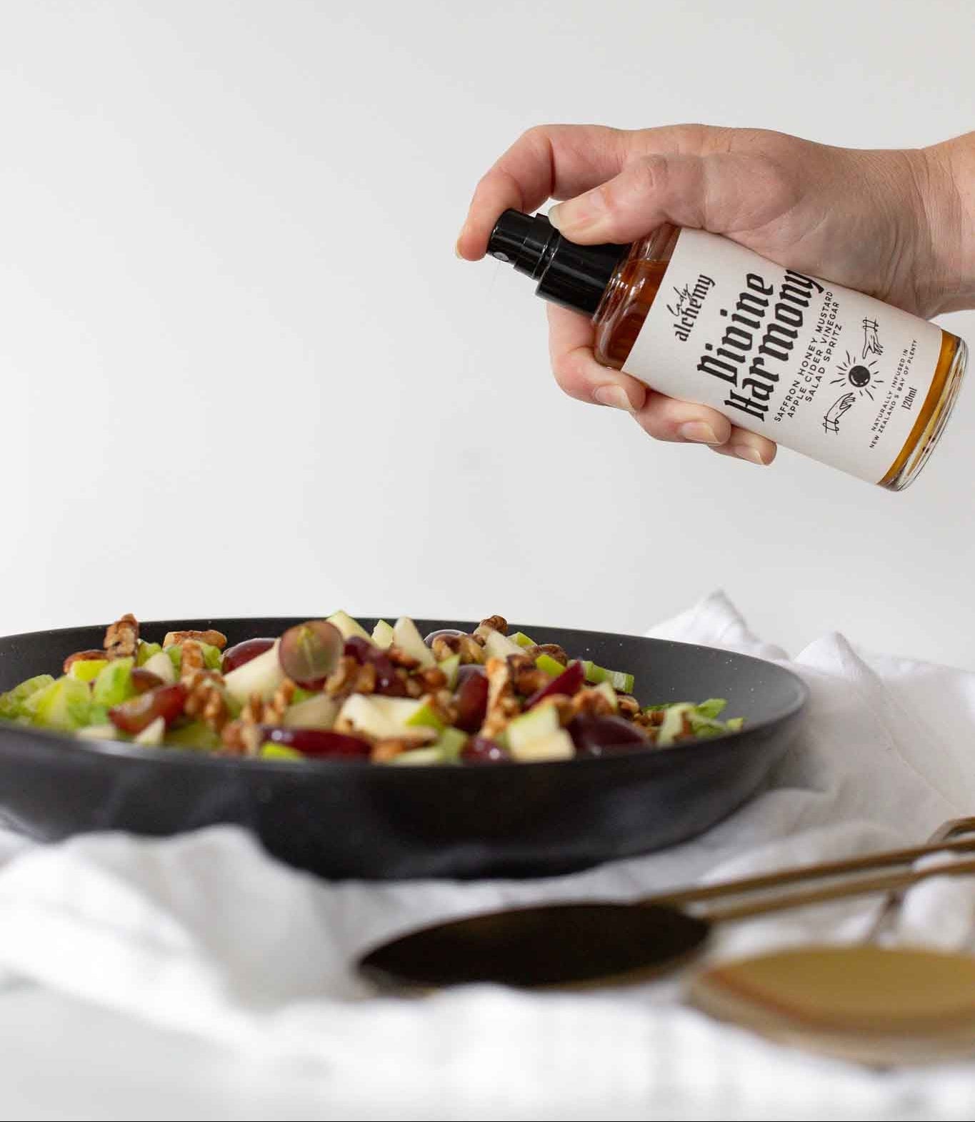 Hand holding a bottle of dressing over a salad on a white background
