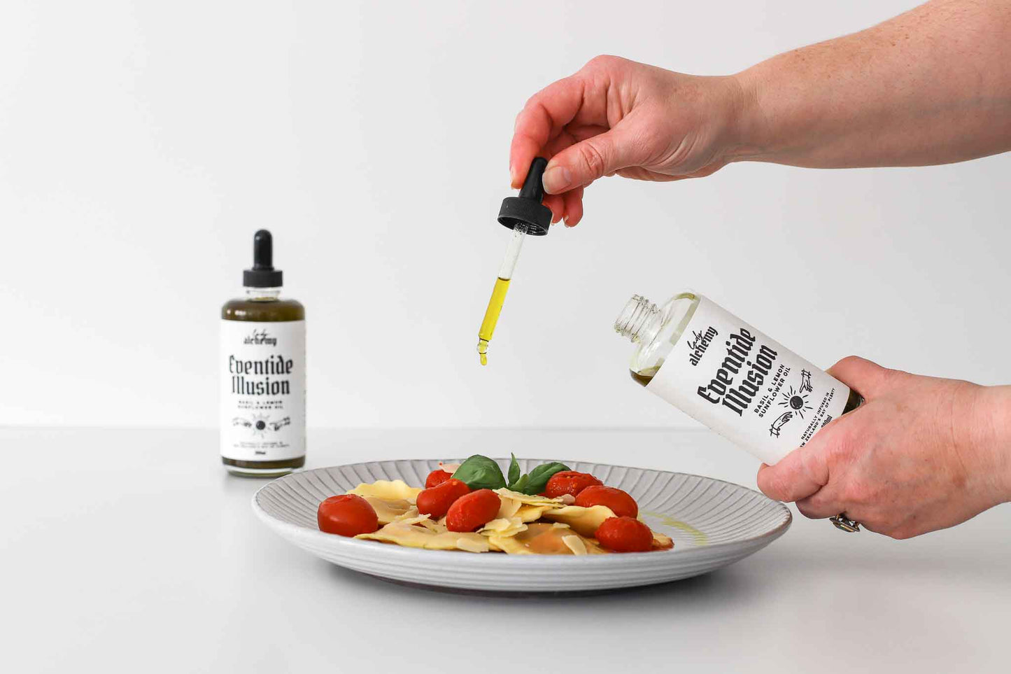 Person drizzling Basil & Lemon oil with a dropper onto a plate of food.